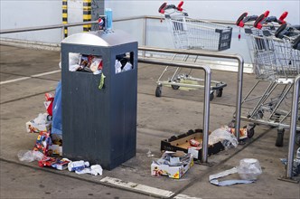 Overflowing dumpster, trash can with plastic bags and cardboard, filthy shopping center,