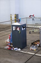 Overflowing dumpster, trash can with plastic bags and cardboard, filthy shopping center,