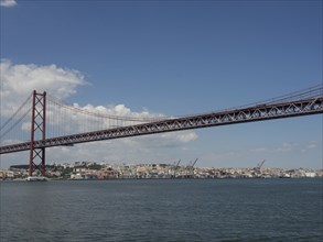 Red bridge over a river with a city in the background and blue sky with few clouds, Lisbon,