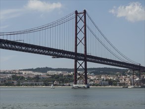 A large suspension bridge over a river with a city in the background, Lisbon, portugal