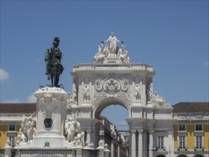 A triumphal arch with an equestrian statue in front of it, surrounded by historic buildings, under