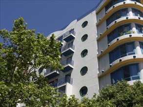 Modern residential building with round windows and balconies, green tree in the foreground, Lisbon,
