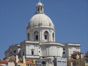 Historic building with large stone dome surrounded by smaller houses under a blue sky, Lisbon,