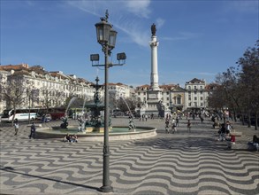 A lively square with a large fountain and a statue, surrounded by historic buildings, Lisbon,