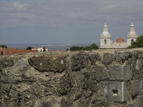 Old stone wall with a view of the city and the sea, buildings and towers in the background, Lisbon,