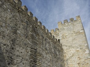 Massive stone walls and a tower of a medieval castle under a blue sky, Lisbon, portugal