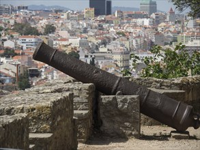 Old cannon on a stone rail, aimed at the city in the background, Lisbon, portugal