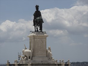 An impressive marble equestrian statue stands on a decorative pedestal under a cloudy sky, Lisbon,
