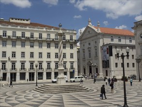 Historic square with a column, surrounded by buildings and a few people under a cloudy sky, Lisbon,