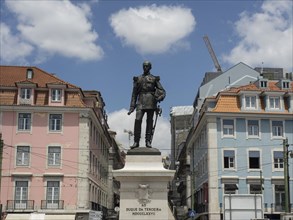 An imposing statue of a historical figure stands between pastel-coloured townhouses against a