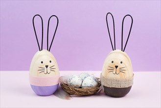 Easter bunny or rabbit sitting next to a wicker nest filled with painted eggs, spring holiday card