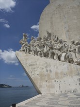 Stone monument with sculptures of historical figures in front of a sky with clouds, Lisbon,
