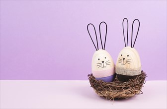 Easter bunny or rabbit couple cuddle together in a wicker nest, wooden egg, spring holiday greeting