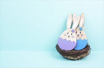 Easter bunny or rabbit couple cuddle together in a wicker nest, wooden egg, spring holiday greeting
