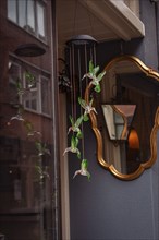 Glass birds in shades of green hang from a ceiling and are reflected in a window. A golden, antique