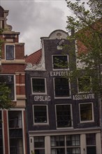 Historic, leaning building with black tiles and red roofs, surrounded by trees, Amsterdam,
