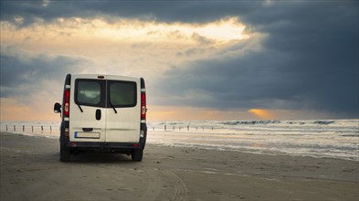 Camper van driving next to the wadden sea at low tide, traveling at the beach of Romo in Denmark,