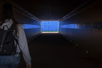 A woman in a dark tunnel walks towards a bright blue exit labelled Waterland, Ilpendam, Netherlands