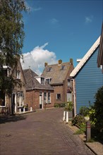 Cobblestone street through a row of traditional houses on a sunny day, Ilpendam, Netherlands