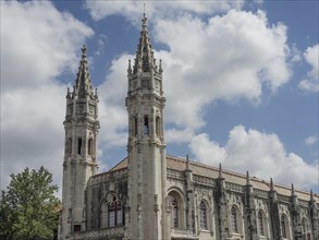 Two gothic steeples of a stone church building under a blue sky with clouds, Lisbon, portugal