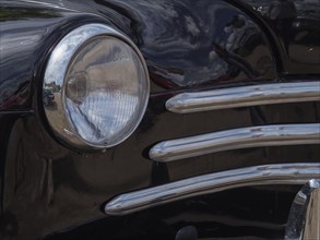Detailed view of a black vintage car, showing the front headlight and chrome trim, winterswijk,