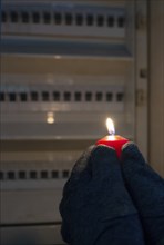 Blackout, standing with a candle in front of a power fuse box, energy cut out, uncertain supply,