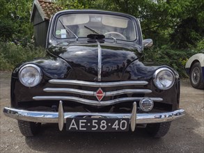 Black vintage car in a forest, showing the front view with licence plate and chrome grill,