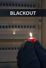 Blackout, standing with a candle in front of a power fuse box, energy cut out, uncertain supply,