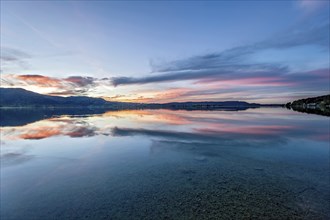 Lake Kochel with reflection of sun and clouds at sunset, calm water, in the background the