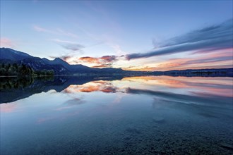 Lake Kochel with reflection of sun and clouds at sunset, calm water, in the background the