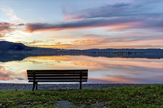 Bench at Lake Kochel, reflection of sun and clouds at sunset, calm water, Kochel am See, Bavarian