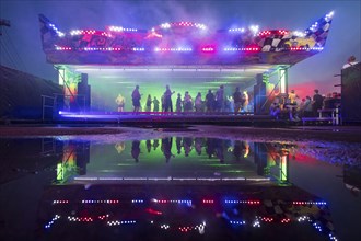 A bumper car with dancing visitors is reflected in a puddle at the Melt Festival in Ferropolis on