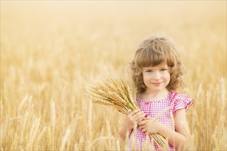 Happy child holding wheat ears against yellow autumn field