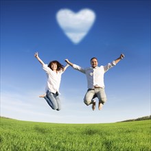 Happy couple jumping in green field against blue sky. Summer vacation concept