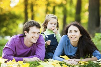 Happy family lying against blurred leaves background in autumn park