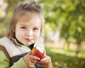 Portrait of happy child eating red apple outdoors in autumn