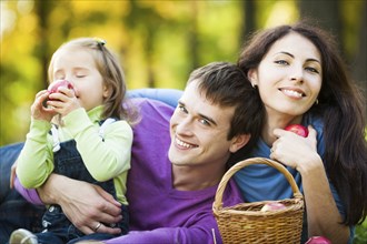 Happy family eating apples in autumn park