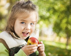 Closeup portrait of happy child eating red apple outdoors in autumn