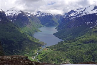 Far-reaching view of a lake between snow-capped mountains and green forests, Lovatnet, Loen,