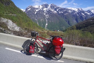 Packed bike on a road in front of snow-covered mountains, a perfect adventure picture in Norwegian