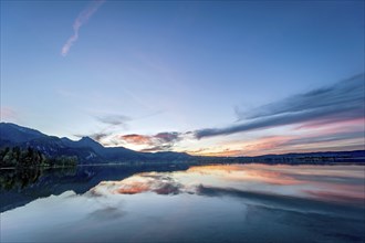 Lake Kochel with reflection of sun and clouds at sunset, calm water, in the background the