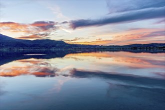 Lake Kochel with reflection of sun and clouds at sunset, calm water, in the background the