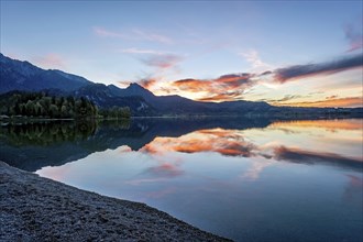 Lake Kochel with reflection of sun and clouds at sunset, calm water, in the background the