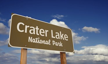 Crater lake national park (oregon) road sign against blue sky and clouds