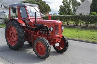 Red vintage tractor, carefully restored oldtimer, driving on the road through the village, motion