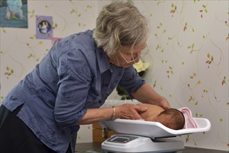 A senior midwife weighs a young baby as part of its post-natal check