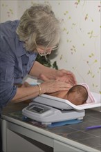 A senior midwife weighs a young baby as part of its post-natal check