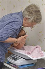 A senior midwife weighs a young baby as part of her post-natal check