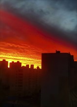 Fiery sunset casting silhouettes of buildings against a dramatic orange and dark sky.Belarus, Minsk