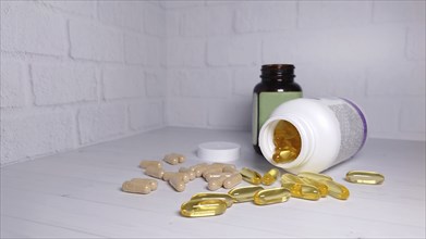 Vitamin and supplement capsules spilled on a white table with brown and white pill bottles